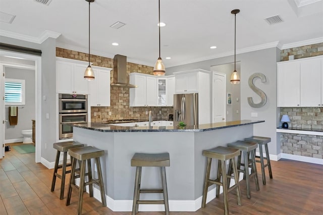 kitchen featuring appliances with stainless steel finishes, hanging light fixtures, dark stone countertops, and wall chimney range hood