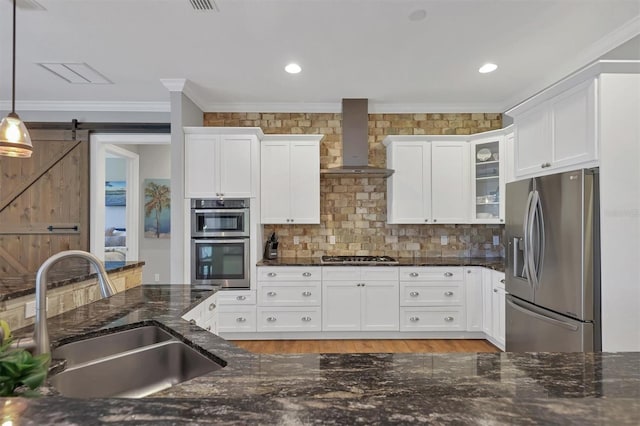 kitchen featuring pendant lighting, wall chimney range hood, sink, a barn door, and appliances with stainless steel finishes