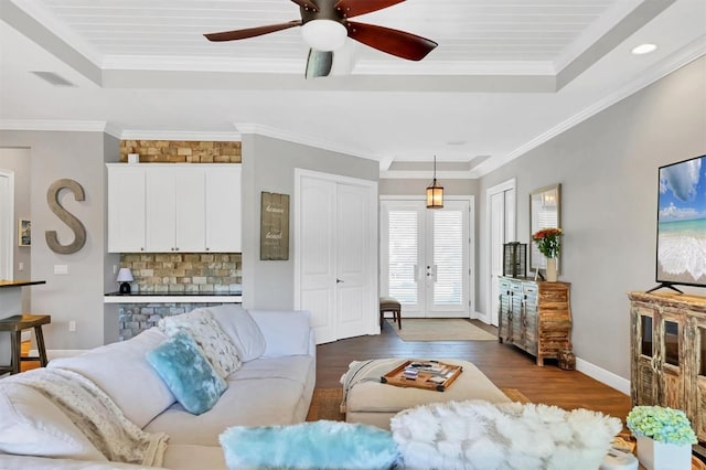 living room with a tray ceiling, dark wood-type flooring, and ornamental molding