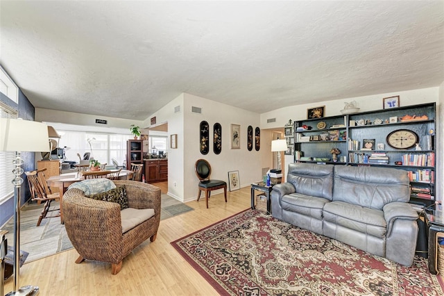 living room featuring vaulted ceiling, a textured ceiling, and light wood-type flooring