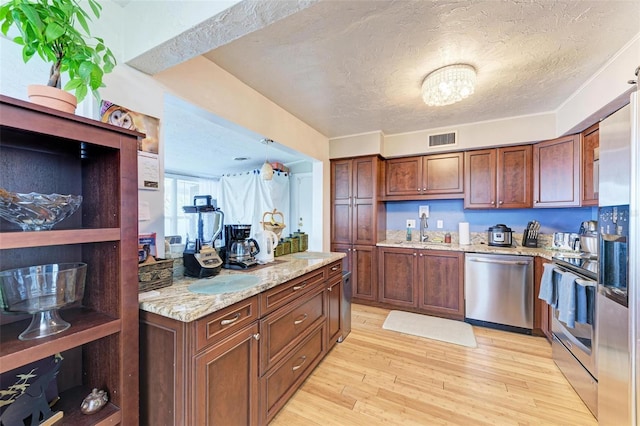 kitchen with appliances with stainless steel finishes, light stone counters, a textured ceiling, sink, and light hardwood / wood-style floors