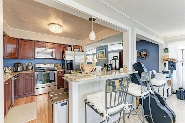 kitchen featuring pendant lighting, light stone countertops, light wood-type flooring, appliances with stainless steel finishes, and a kitchen bar