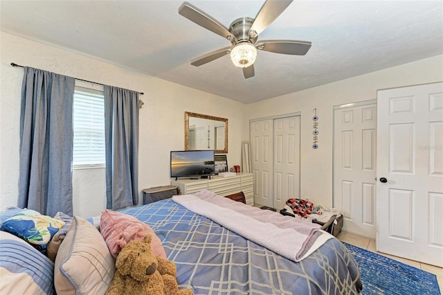 tiled bedroom featuring a textured ceiling, two closets, and ceiling fan