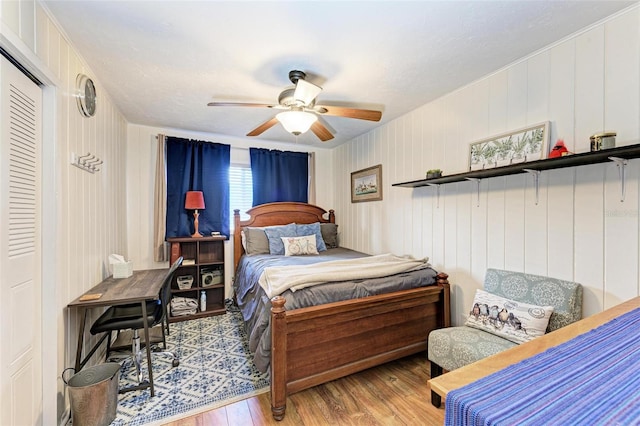 bedroom with light wood-type flooring, a textured ceiling, ceiling fan, wooden walls, and a closet