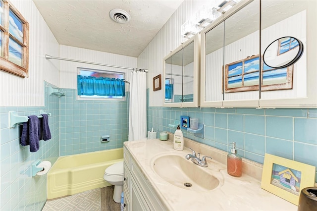 full bathroom with vanity, toilet, a textured ceiling, tile walls, and shower / tub combo