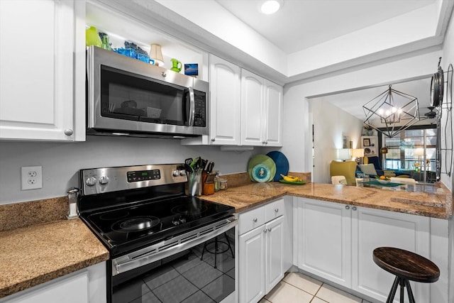 kitchen with appliances with stainless steel finishes, light tile patterned floors, a notable chandelier, dark stone countertops, and white cabinetry