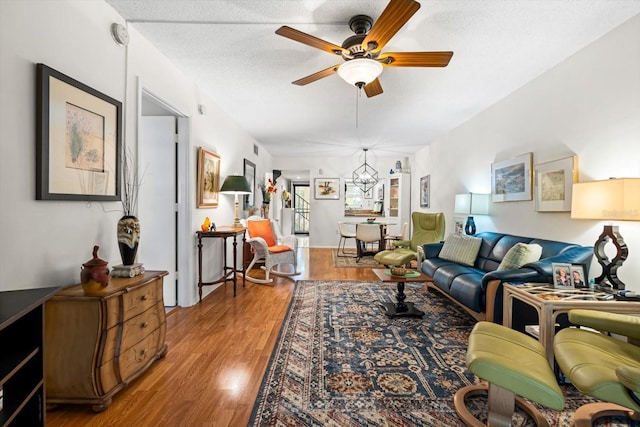 living room featuring hardwood / wood-style floors, ceiling fan with notable chandelier, and a textured ceiling