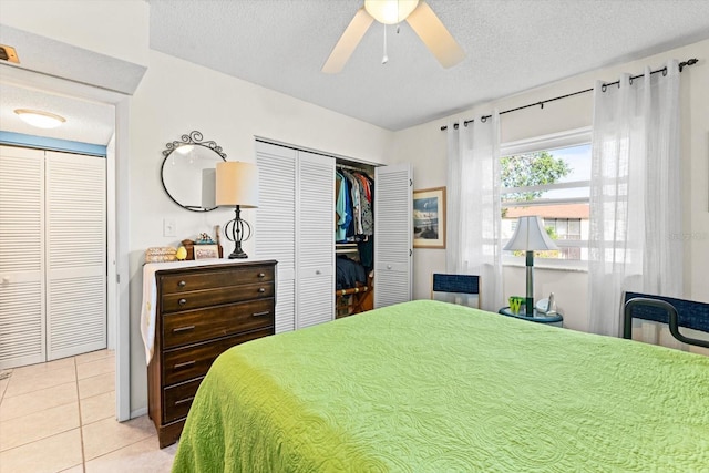 tiled bedroom with ceiling fan, a textured ceiling, and two closets