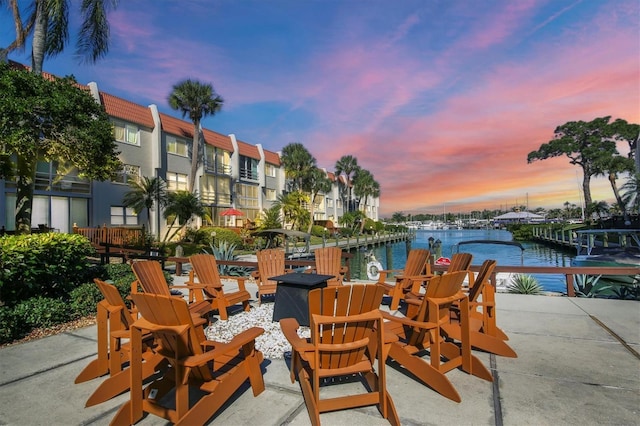 patio terrace at dusk featuring a water view and a dock