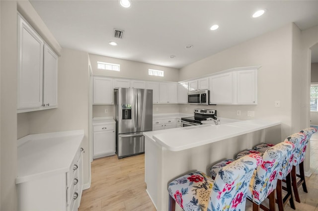 kitchen with white cabinetry, stainless steel appliances, kitchen peninsula, a breakfast bar area, and light wood-type flooring