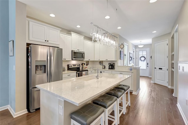 kitchen featuring light stone countertops, stainless steel appliances, decorative light fixtures, a center island, and white cabinetry