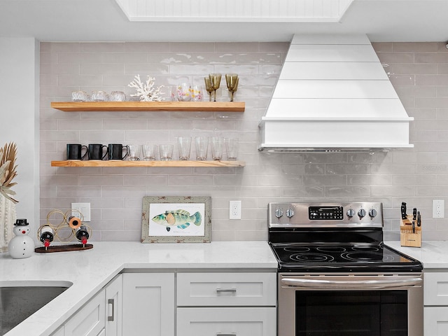 kitchen with white cabinets, backsplash, light stone counters, and stainless steel range with electric stovetop