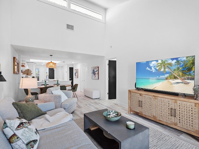 living room featuring a high ceiling, light hardwood / wood-style floors, and a healthy amount of sunlight