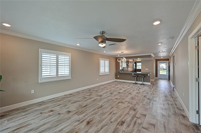 unfurnished living room with sink, crown molding, ceiling fan, light wood-type flooring, and a textured ceiling