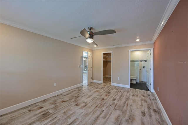 unfurnished bedroom with ceiling fan, ensuite bathroom, a walk in closet, a closet, and light wood-type flooring