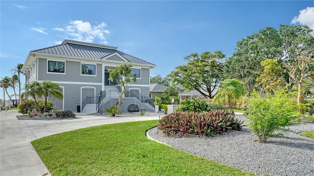 raised beach house featuring driveway, metal roof, a front lawn, and a standing seam roof