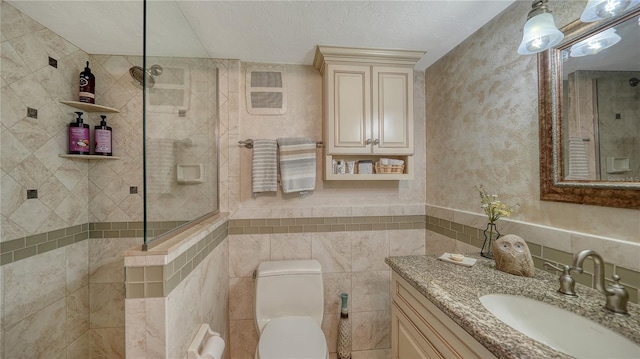 bathroom with a tile shower, vanity, a textured ceiling, tile walls, and toilet