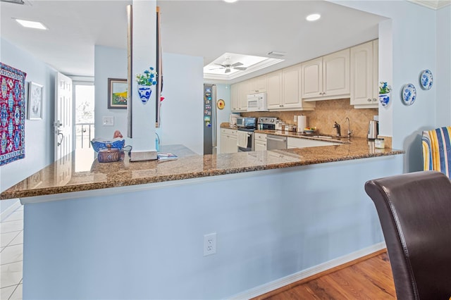 kitchen featuring dark stone counters, kitchen peninsula, light hardwood / wood-style flooring, and stainless steel appliances