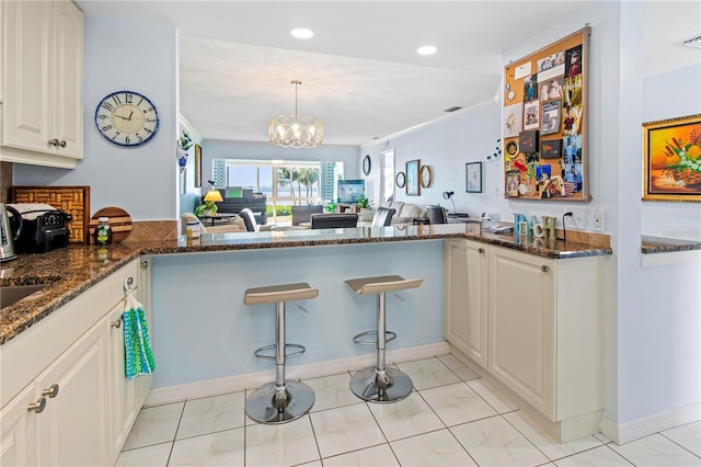 kitchen featuring dark stone counters, an inviting chandelier, hanging light fixtures, kitchen peninsula, and white cabinetry