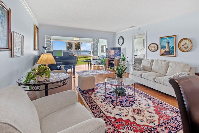 living room with ceiling fan, wood-type flooring, a textured ceiling, and ornamental molding