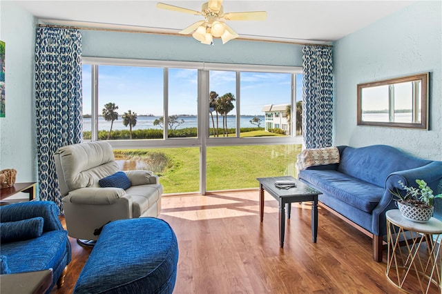 living room featuring hardwood / wood-style flooring, ceiling fan, and a water view