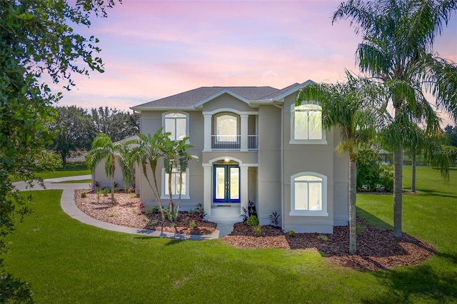 view of front of home with a balcony, a yard, and french doors