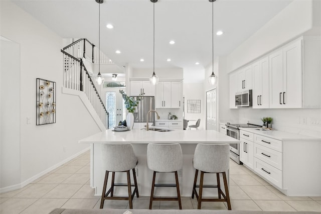 kitchen featuring stainless steel appliances, sink, decorative light fixtures, white cabinetry, and an island with sink