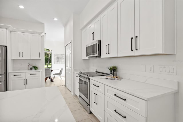 kitchen with white cabinets, light tile patterned floors, stainless steel appliances, and light stone countertops