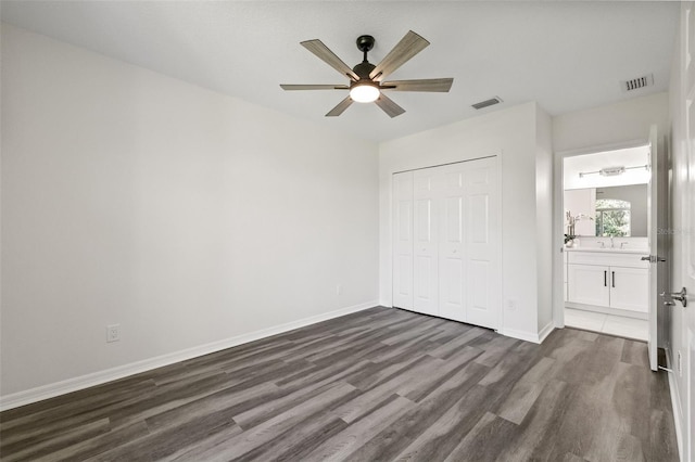 unfurnished bedroom featuring ensuite bathroom, ceiling fan, sink, dark hardwood / wood-style floors, and a closet