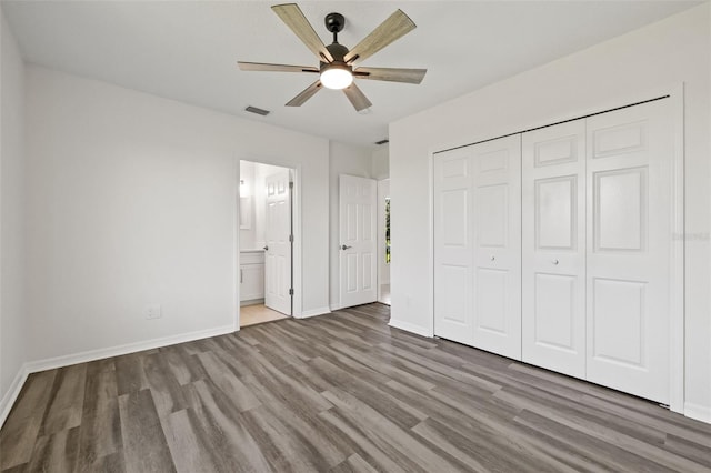 unfurnished bedroom with a closet, ceiling fan, ensuite bathroom, and wood-type flooring