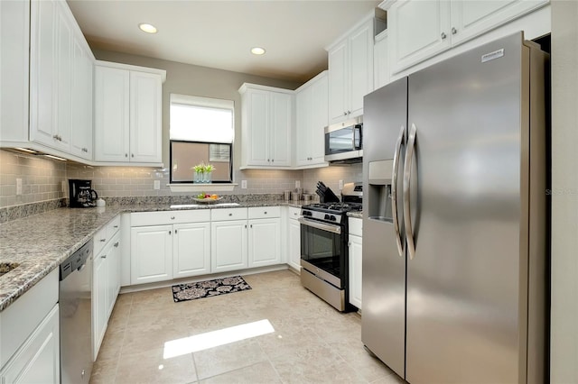 kitchen featuring appliances with stainless steel finishes, tasteful backsplash, light stone counters, white cabinetry, and light tile patterned flooring