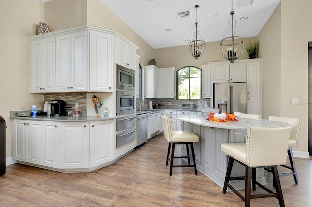 kitchen featuring decorative backsplash, appliances with stainless steel finishes, a kitchen island, decorative light fixtures, and white cabinetry