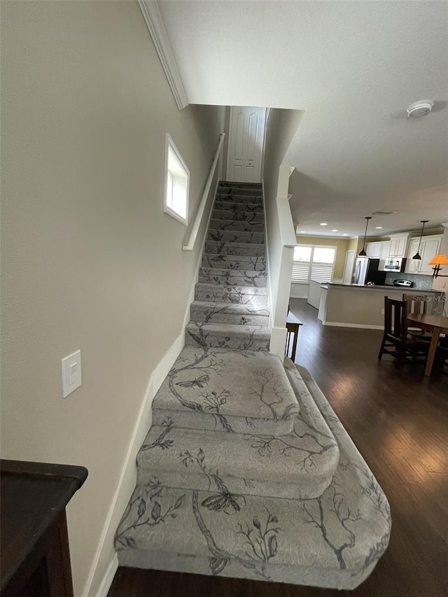 stairs with hardwood / wood-style flooring and crown molding