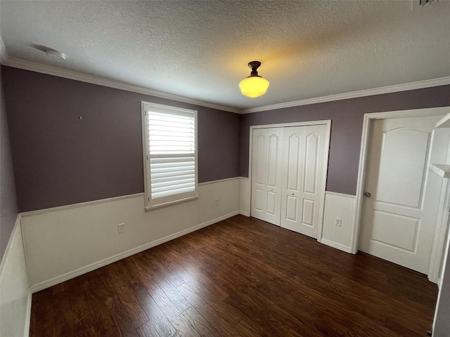 unfurnished bedroom with a textured ceiling, crown molding, dark wood-type flooring, and a closet