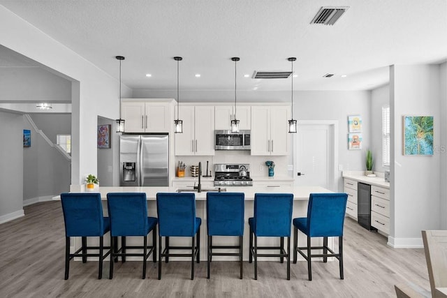 kitchen featuring white cabinets, pendant lighting, light wood-type flooring, and appliances with stainless steel finishes