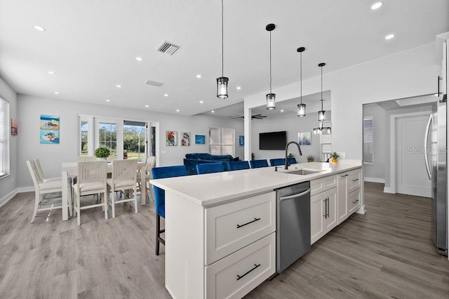 kitchen with sink, appliances with stainless steel finishes, a kitchen island with sink, white cabinets, and light wood-type flooring