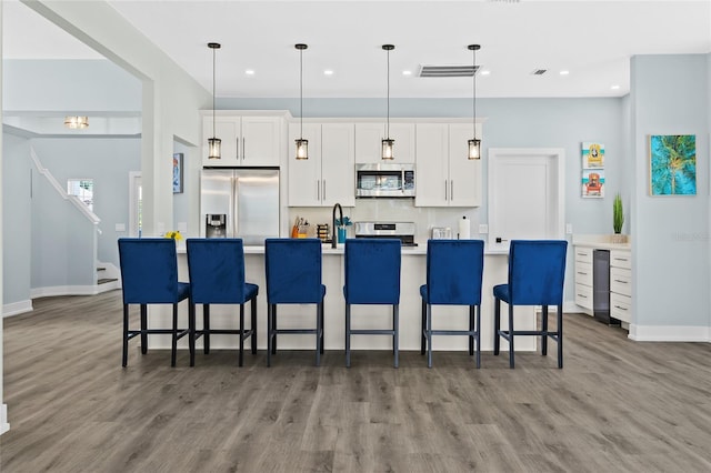 kitchen featuring stainless steel appliances, decorative light fixtures, a center island with sink, white cabinets, and dark hardwood / wood-style floors