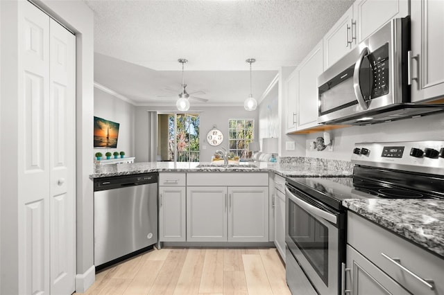 kitchen with a textured ceiling, light wood-style flooring, stainless steel appliances, a sink, and ornamental molding