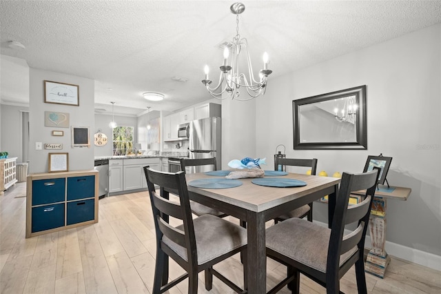 dining area with light wood-style floors, a notable chandelier, a textured ceiling, and baseboards