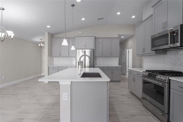 kitchen featuring sink, hanging light fixtures, vaulted ceiling, a center island with sink, and appliances with stainless steel finishes