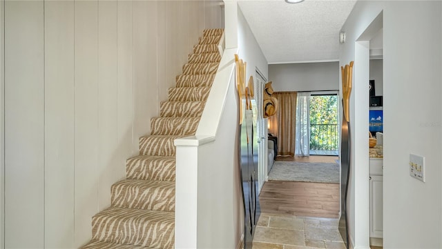 stairway featuring crown molding, wood-type flooring, and a textured ceiling