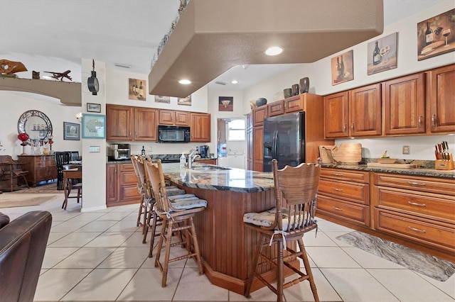 kitchen with fridge with ice dispenser, a kitchen island with sink, a breakfast bar, and light tile patterned flooring