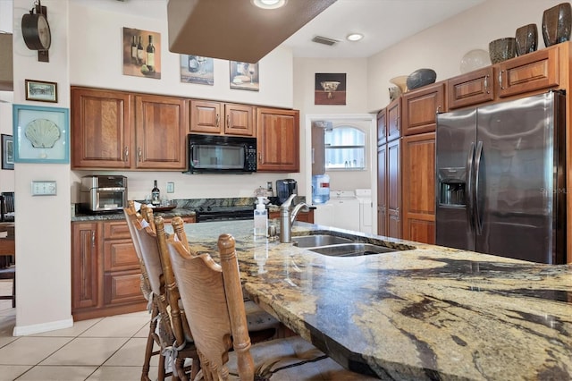 kitchen with stainless steel refrigerator with ice dispenser, independent washer and dryer, dark stone countertops, a breakfast bar area, and light tile patterned flooring