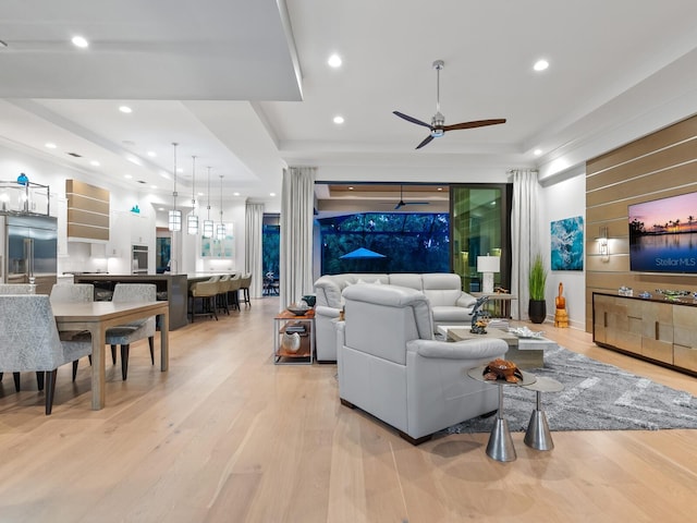 living room with ceiling fan, light wood-type flooring, and a tray ceiling