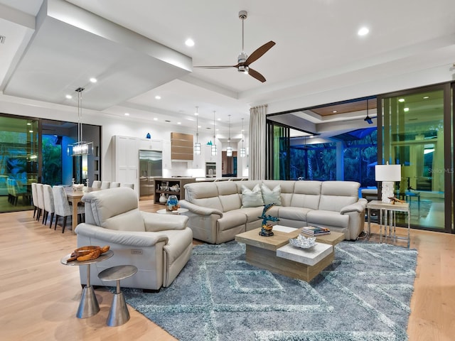 living room with a raised ceiling, light hardwood / wood-style flooring, and ceiling fan