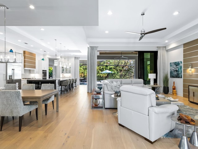 living room featuring ceiling fan with notable chandelier, light wood-type flooring, and a tray ceiling