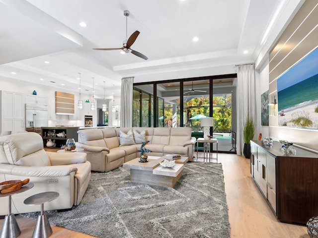 living room featuring a raised ceiling, ceiling fan, and light wood-type flooring