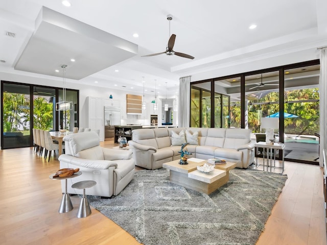 living room featuring a tray ceiling, ceiling fan, and light hardwood / wood-style flooring