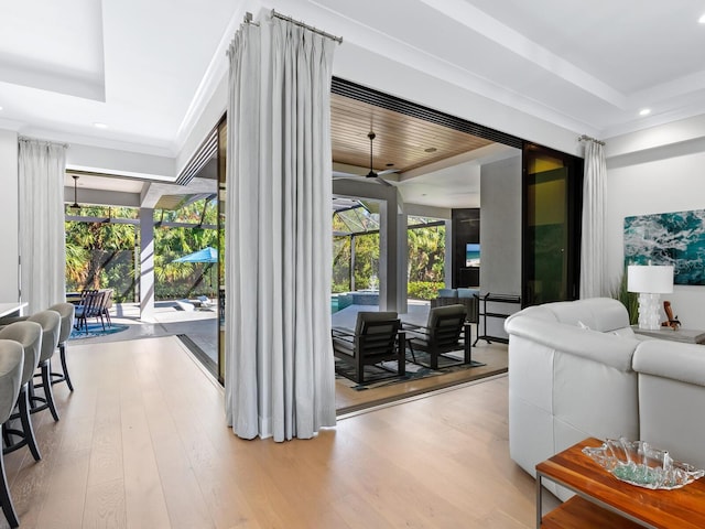 living room with light wood-type flooring, a raised ceiling, and a healthy amount of sunlight