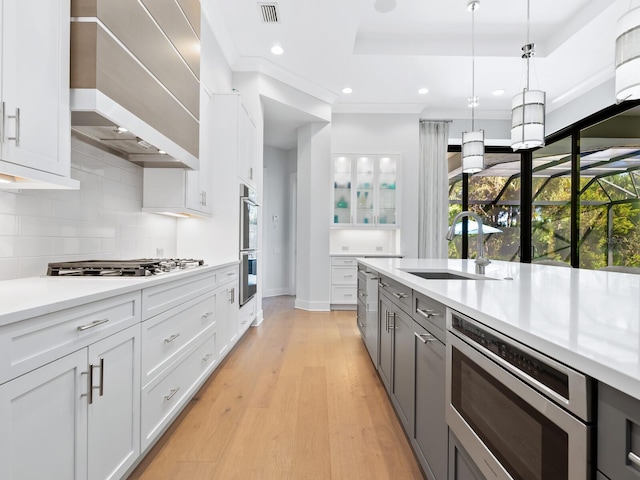 kitchen featuring white cabinetry, sink, stainless steel appliances, light hardwood / wood-style floors, and custom range hood